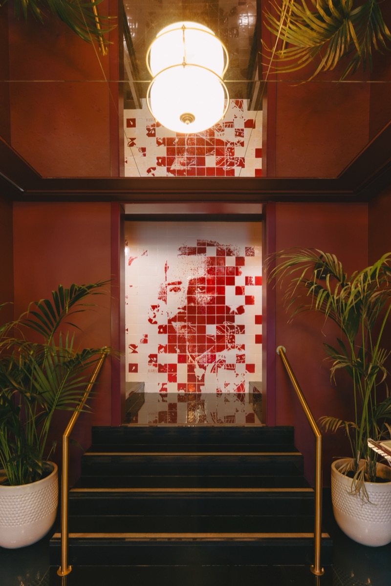 Red-and-white carved-tile portrait panel rising over the stairwell at Hotel 1904 Benfica, flanked by palms
