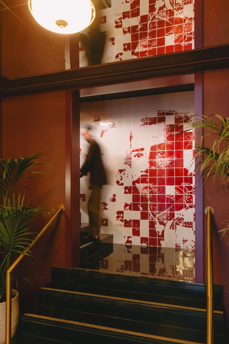 The tile panel seen from the stair landing, a guest passing