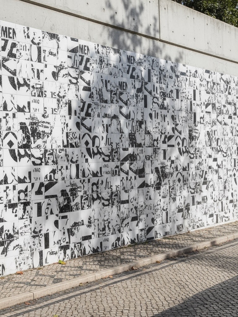 Draft visualisation — street wall in Vhils black-and-white newsprint-collage tiles, dappled light