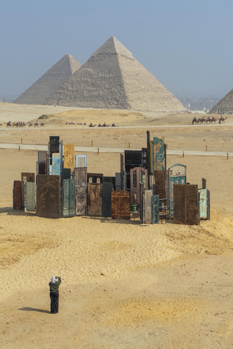 Elevated view of the monument with camels and the pyramids beyond
