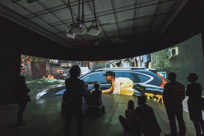 Crowd before a video projection and carved car at Le Centquatre-Paris