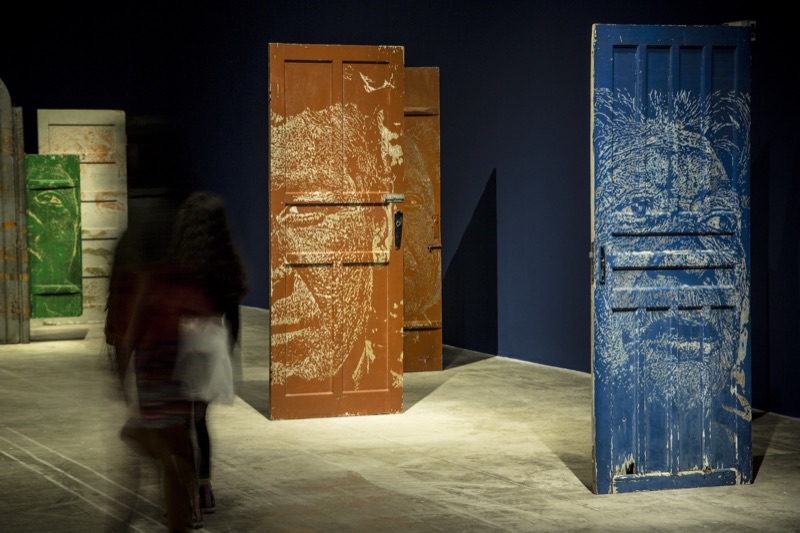 Blue and orange carved Guarani-portrait doors with visitors in motion blur, Brasília