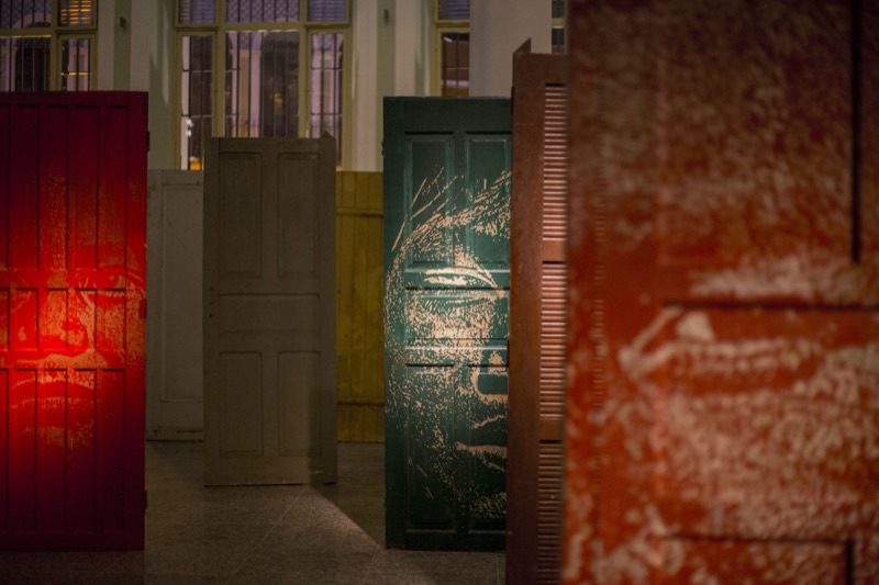 Carved Guarani-portrait doors among plain doors, night install view, CAIXA Cultural Recife